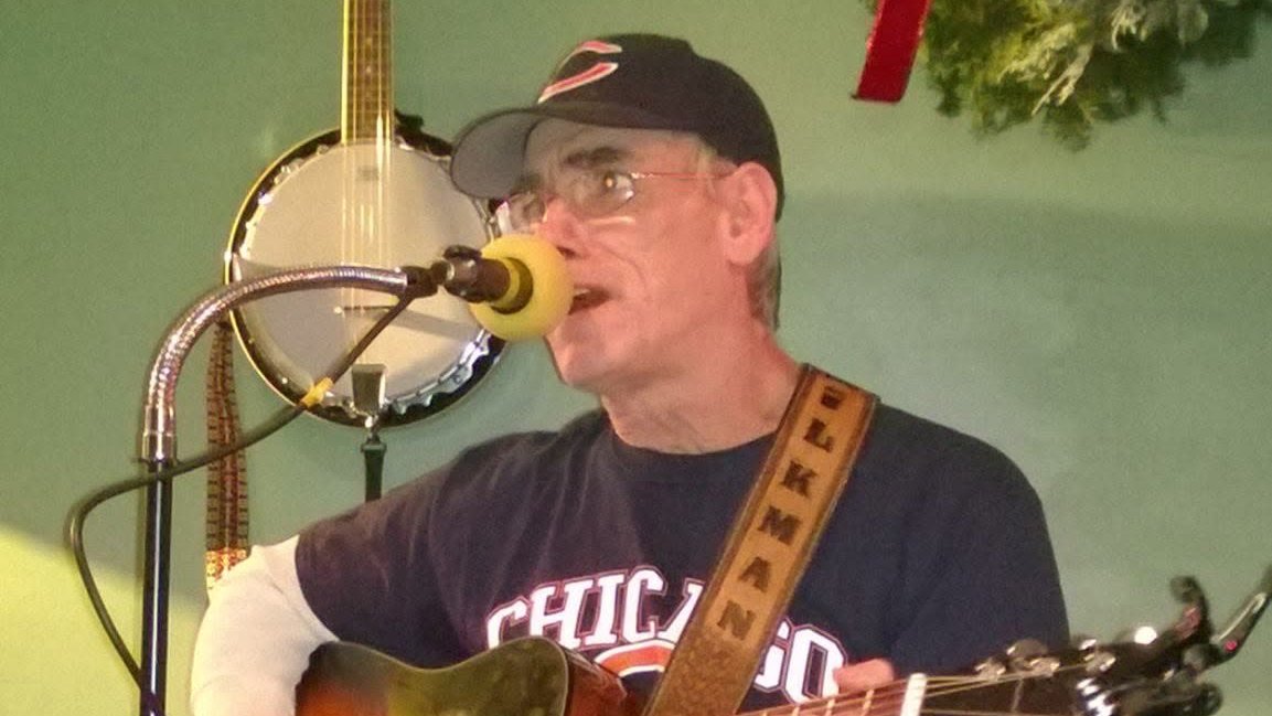 Mike Bollig singing into a microphone while playing acoustic guitar
